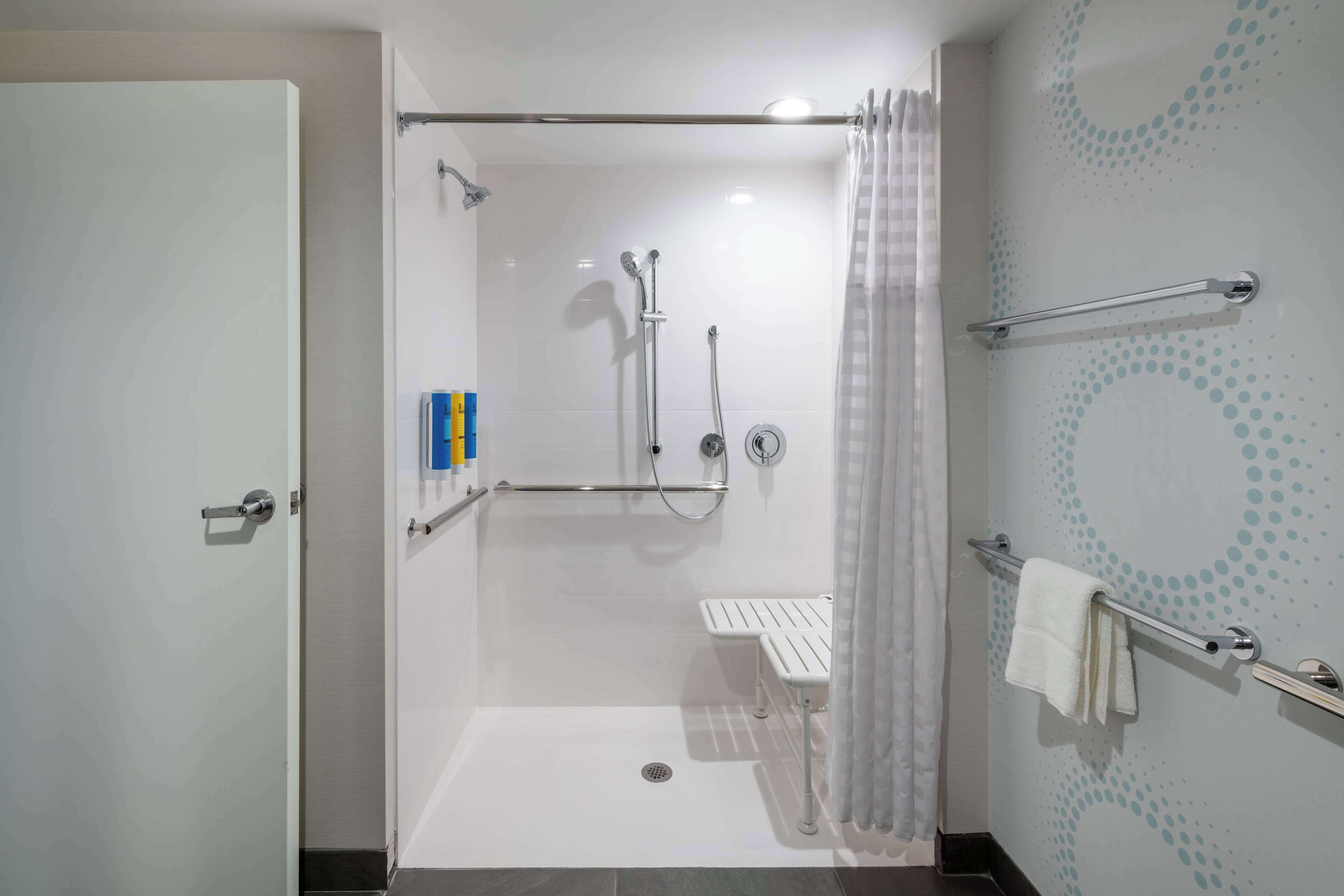A modern bathroom with a walk-in shower, grab bars, a bench, and a towel rack.