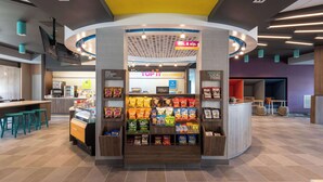 A snack kiosk with a variety of chips and snacks, a seating area with stools, and a counter with a menu. - Tru By Hilton Fayetteville Fort Bragg (Fayetteville)