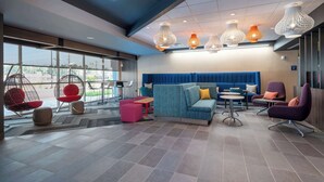 A modern lounge area with seating, a blue sofa, and hanging light fixtures. - Tru By Hilton Fayetteville Fort Bragg (Fayetteville)