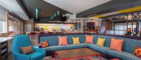 A modern lobby with a blue sofa, red coffee table, and pink ottoman.