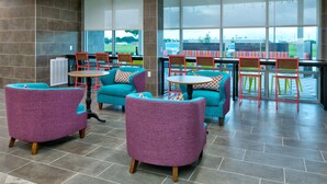 Een moderne zithoek binnen met paarse en teal stoelen, een klein rond tafeltje en grote ramen met uitzicht op het buiten.