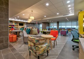 Un espacio interior moderno con diversas zonas de estar, incluyendo un sofá y sillones, así como una mesa de comedor. Amplias ventanas ofrecen luz natural y vistas al exterior.