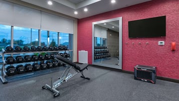 Uma academia com equipamentos de musculação, um banco e um espelho na parede.