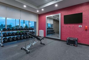 Uma academia com equipamentos de musculação, um banco e um espelho na parede.