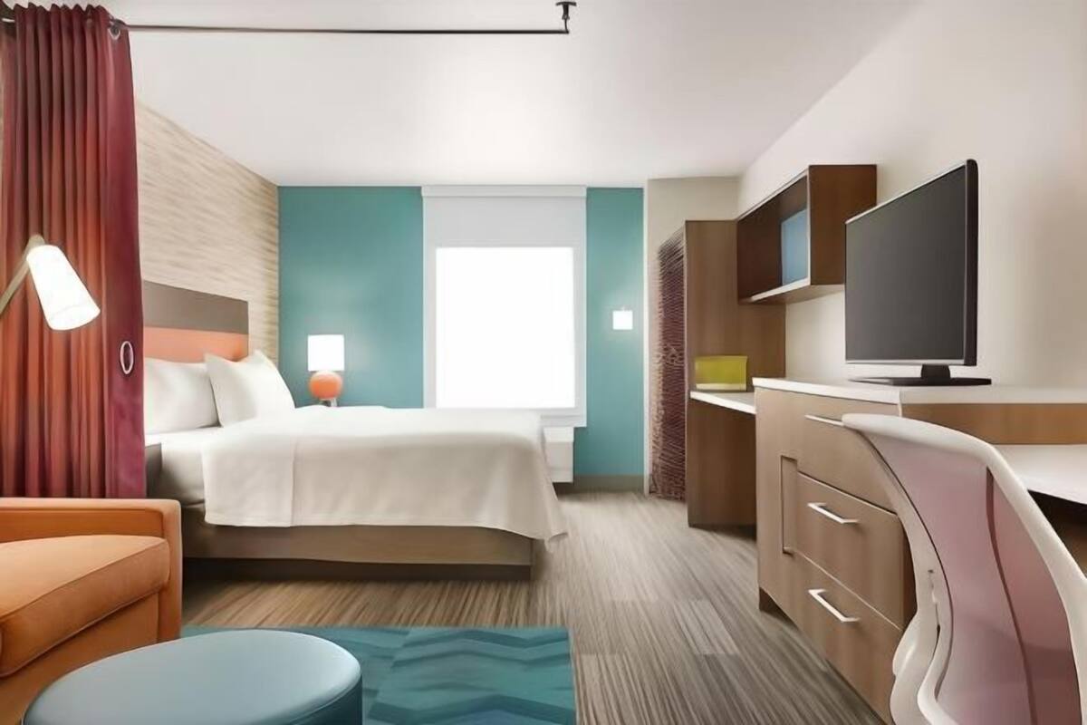 Een hotelkamer met een bed, een bureau met een televisie, een lamp en een raam.