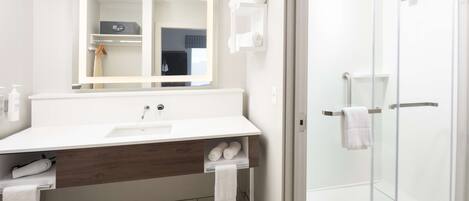 A modern bathroom with a white sink, mirror, and glass shower enclosure.