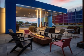 An outdoor seating area with chairs and a fire feature, under a covered structure with a view of a building in the background.