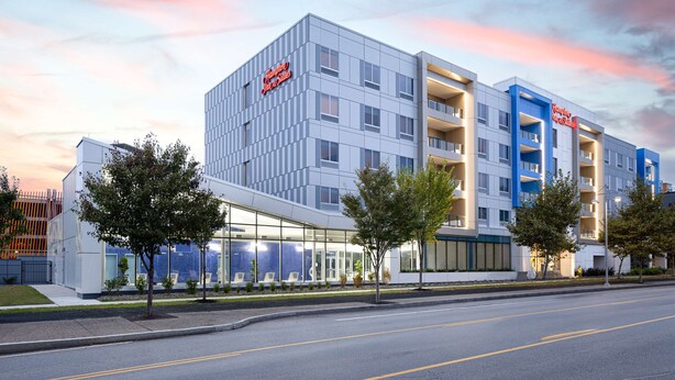 A modern hotel with a glass facade, multiple balconies, and a clear sky at dusk. - Hampton Inn & Suites Rochester Downtown (Rochester)