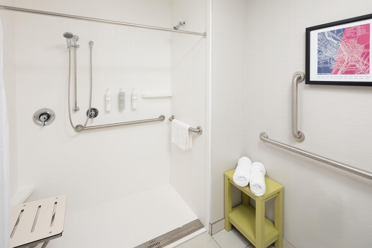 A modern bathroom with a shower, grab bars, a towel rack, and a small shelf with toiletries.