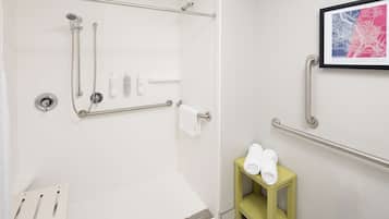 Un baño moderno con cabina de ducha de vidrio, secamanos, toallero y un pequeño estante amarillo con toallas.