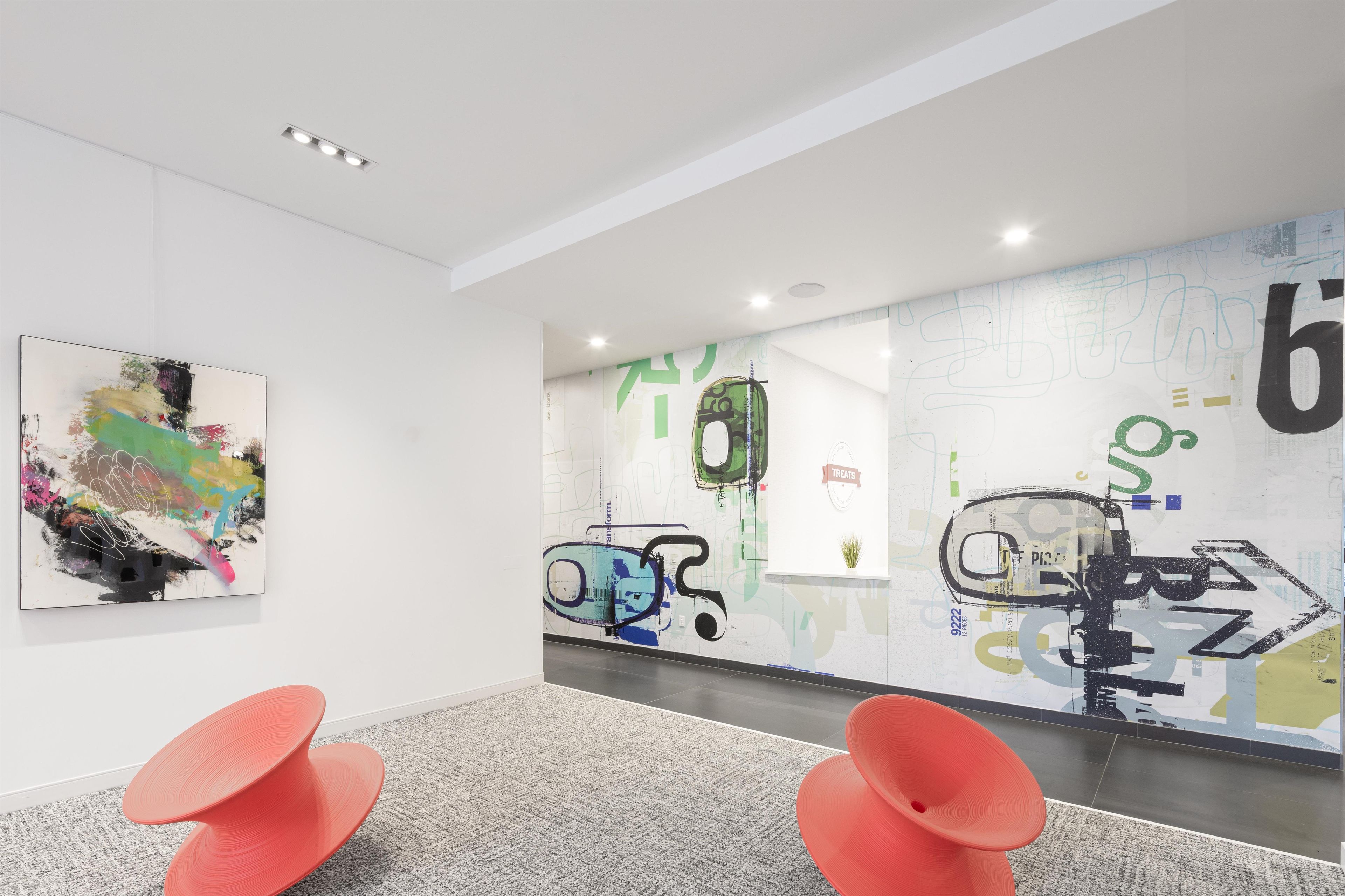 A modern interior with a minimalist design, featuring a large abstract painting, a wall with graffiti-style artwork, and a pair of orange chairs.