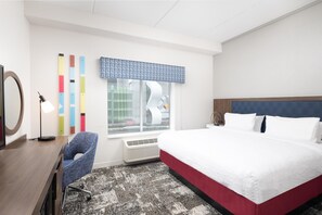 A hotel room with a bed, a desk, a chair, a window with a view, and a patterned carpet.