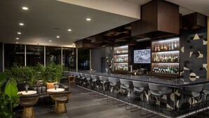 A modern bar area with a long counter, bar stools, and a large display screen.