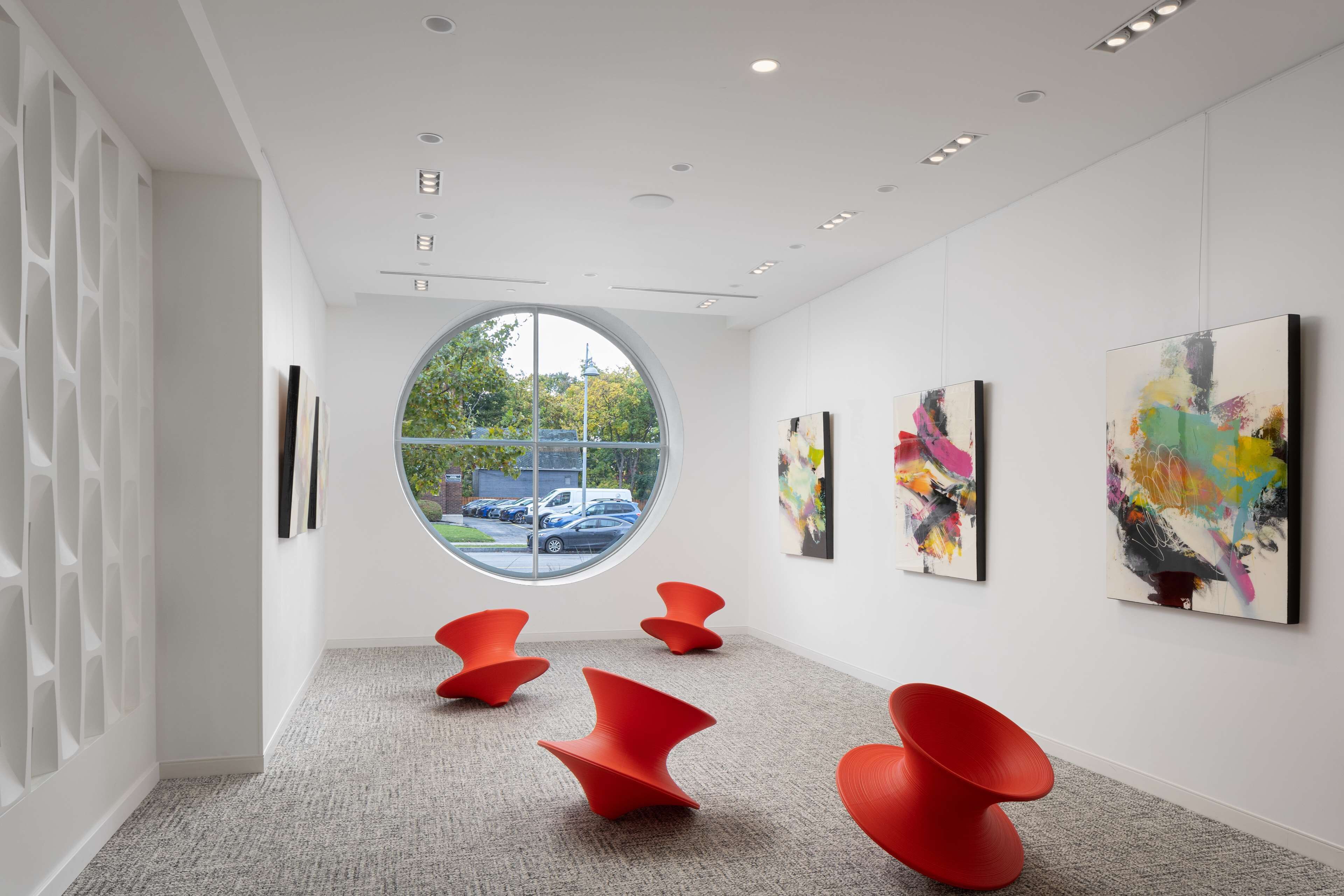 A modern art gallery with a circular skylight, red chairs, and abstract paintings on the walls.