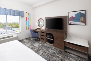 Hotellihuone, jossa on sänky, työpöytä, taulutelevisio, mikroaaltouuni ja ikkuna, josta on näkymä rakennuksiin.