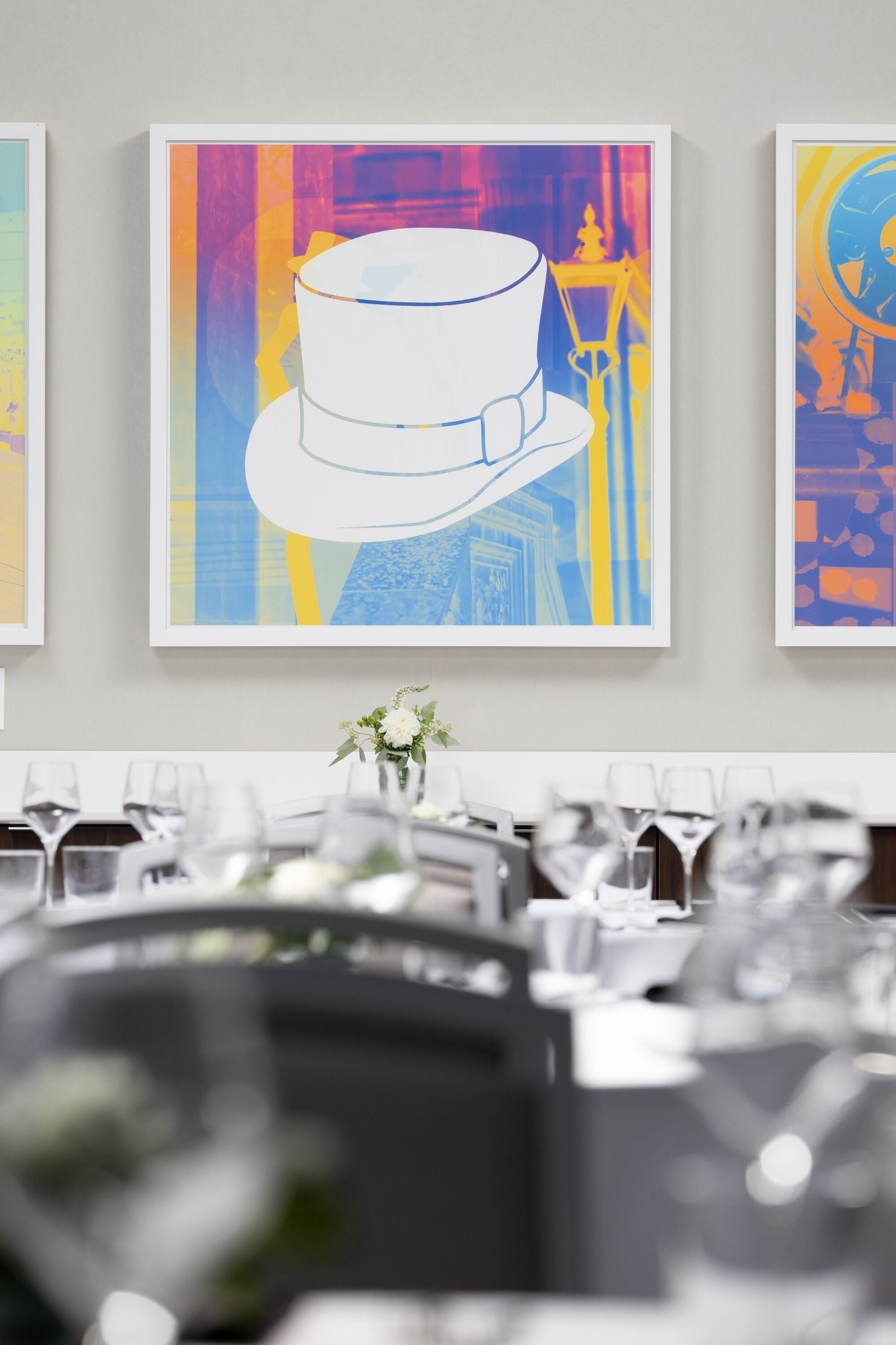 A dining area with a table set for a meal, a vase with flowers, and three framed artworks on the wall.