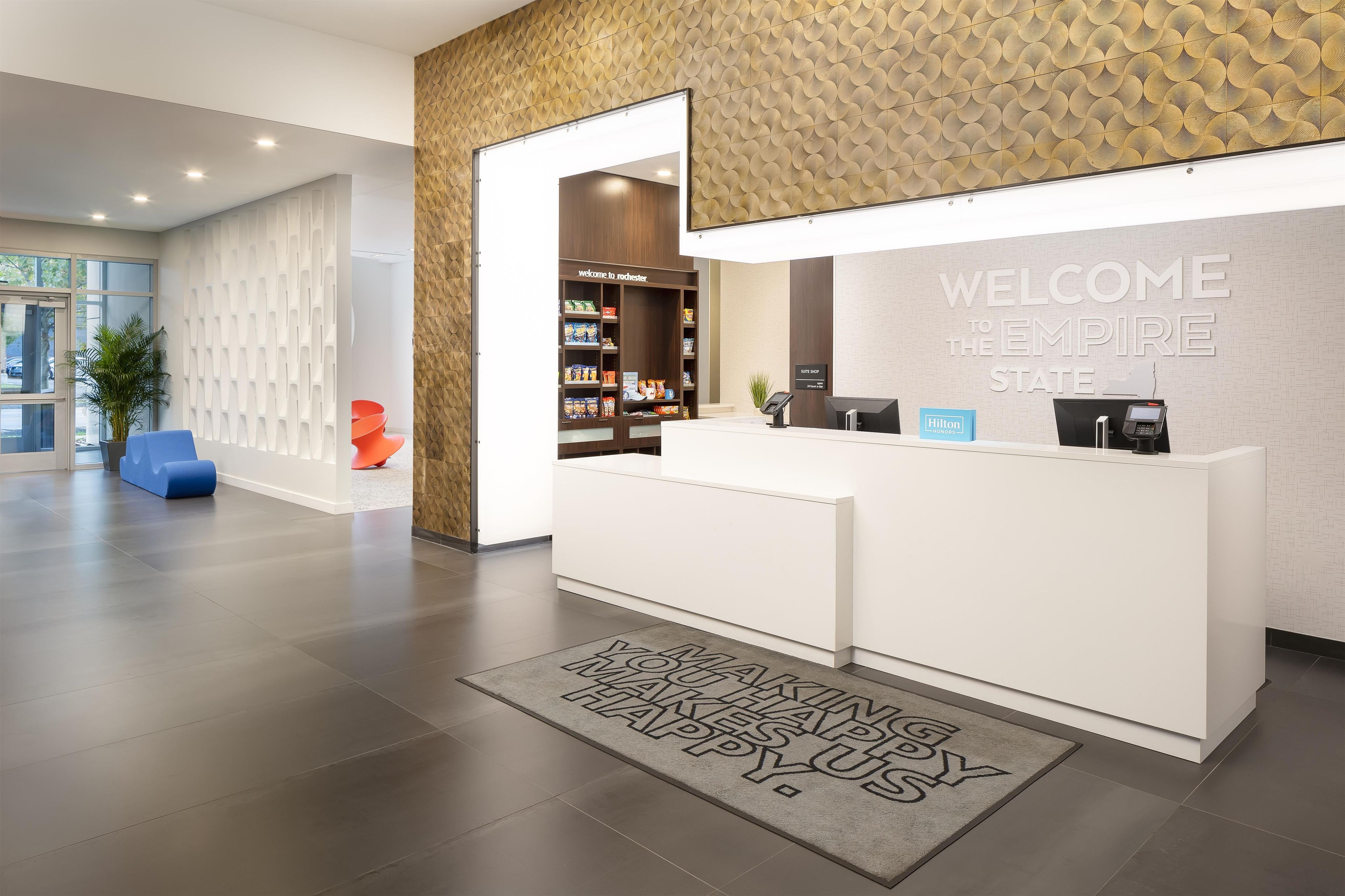 Un comptoir d’accueil d’hôtel avec une pancarte « Bienvenue à l’Empire State », une boutique de luxe et un tapis sur lequel est écrit « Merci ».