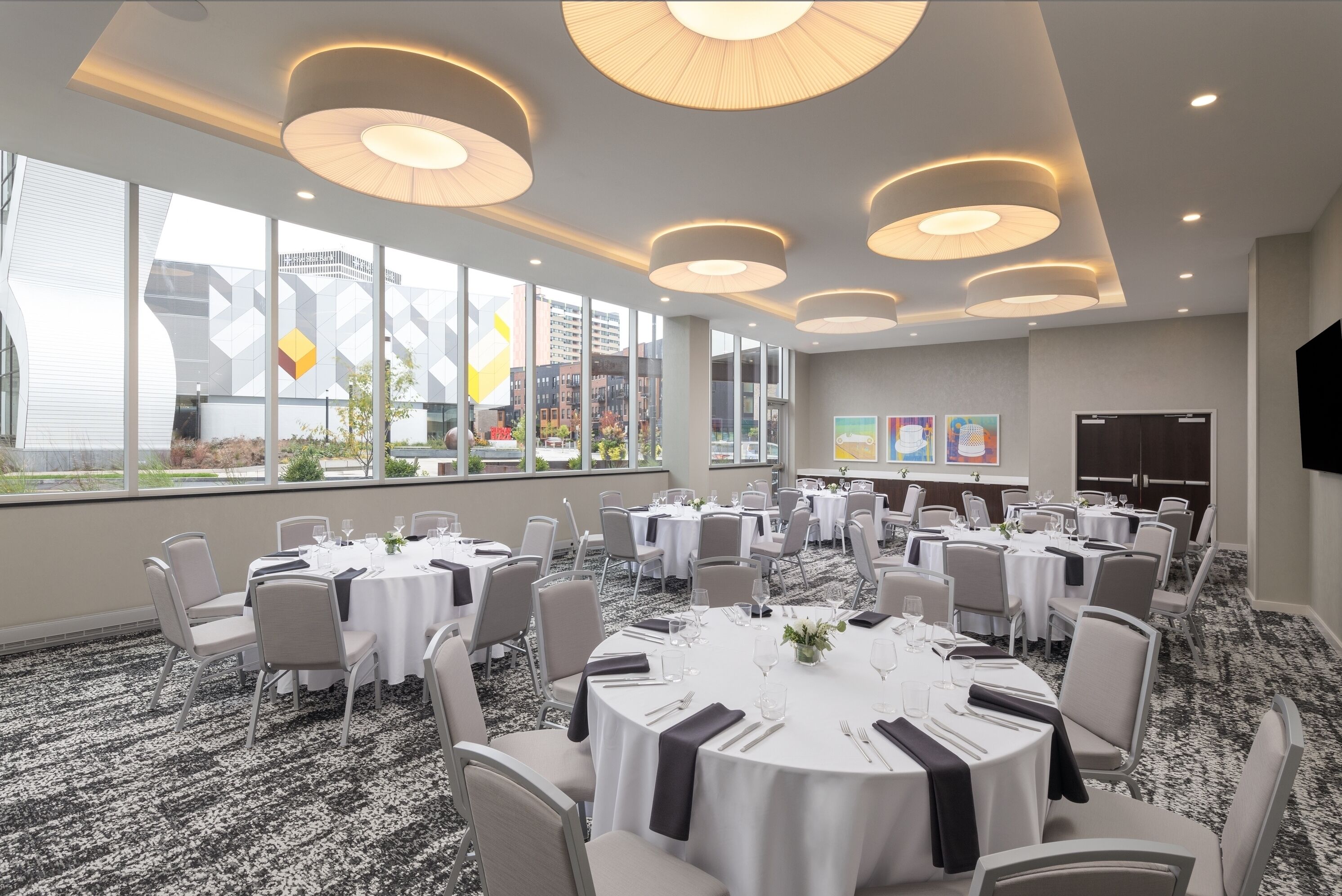 Een vergaderzaal met ronde tafels, witte tafelkleden en grijze stoelen.