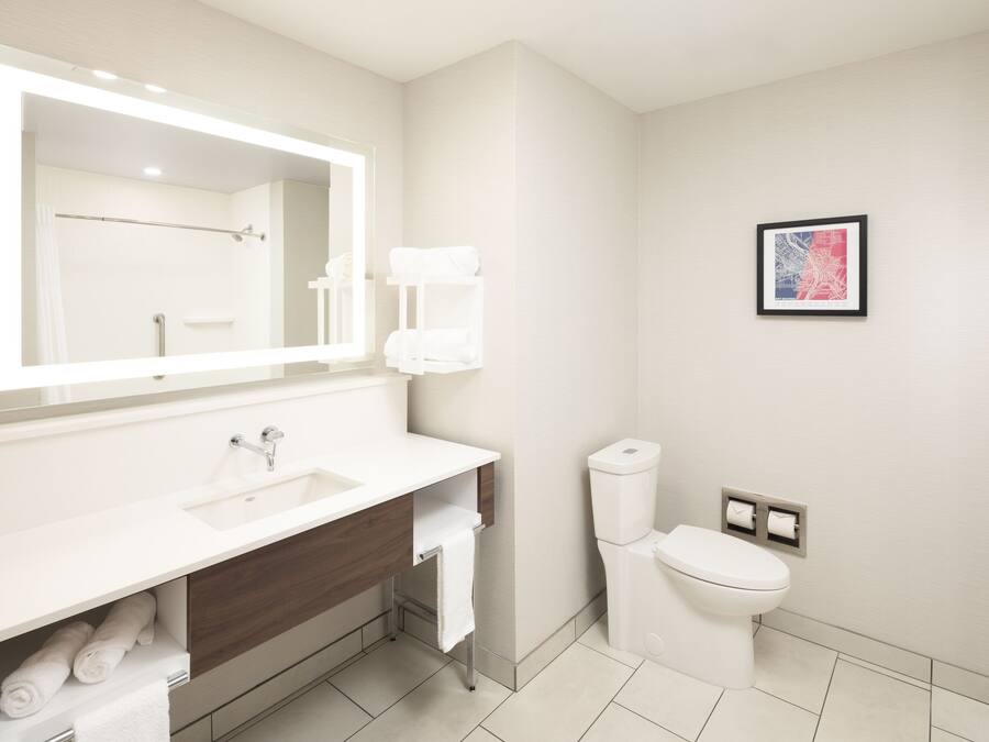 Un baño moderno con un espejo grande, lavamanos blanco y retrete.