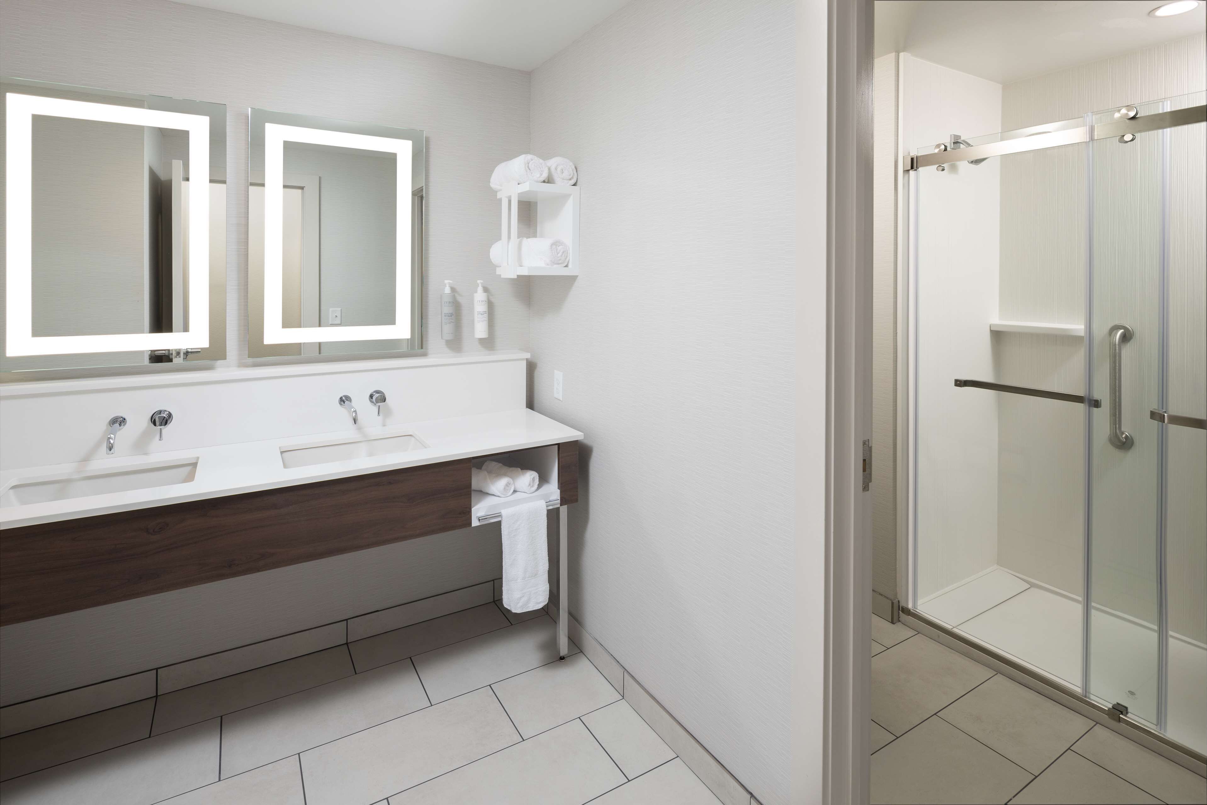 A modern bathroom with two sinks, a mirror, and a glass shower enclosure.