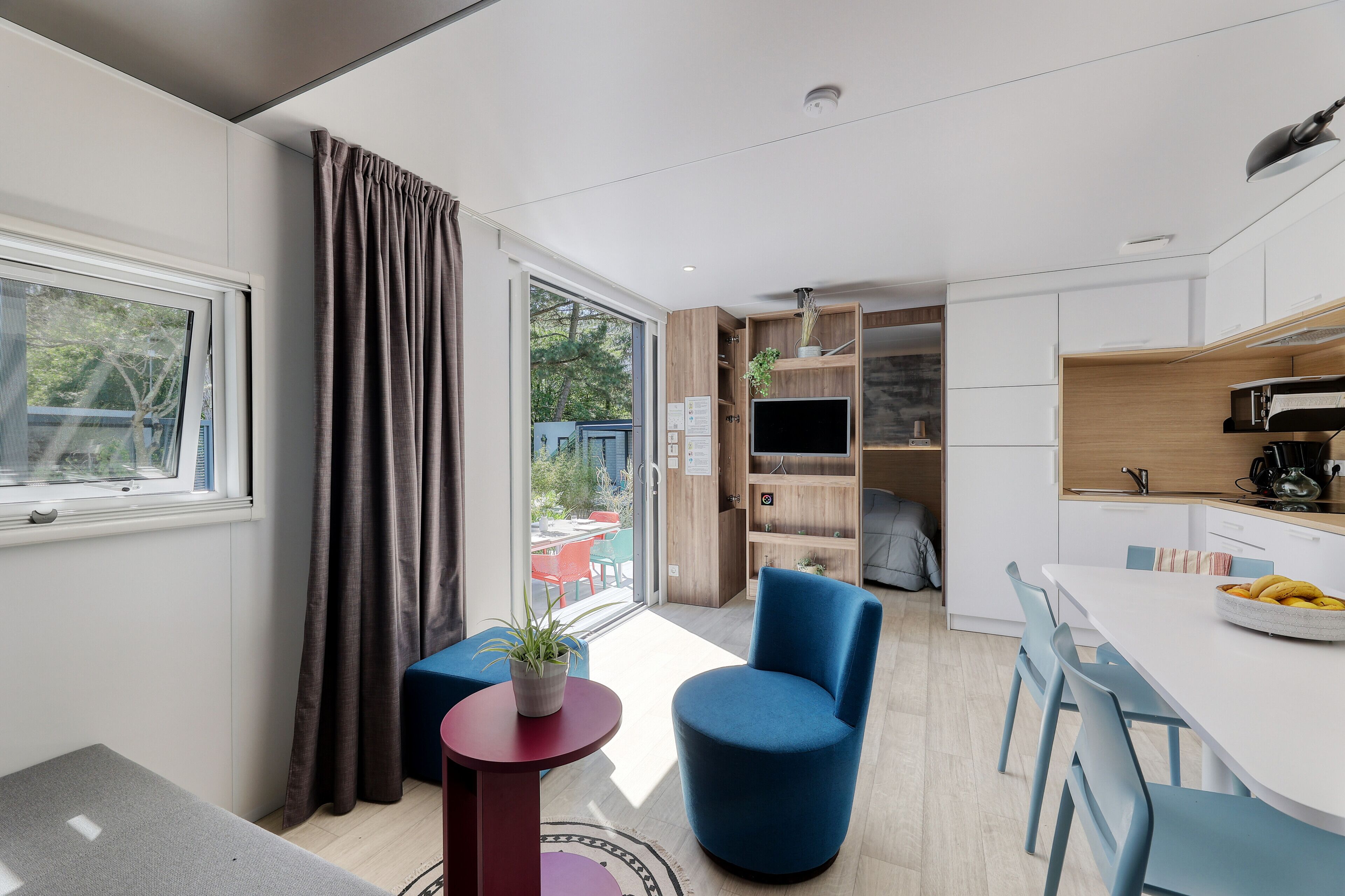 A modern kitchen with a dining area, a blue chair, and a small table with a plant.