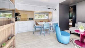 A modern kitchen with white cabinets, a dining area with blue chairs, and a view of the outdoors through a window. - Le Carrousel, Premium 4 persons in Nantes Camping***** (Nantes)