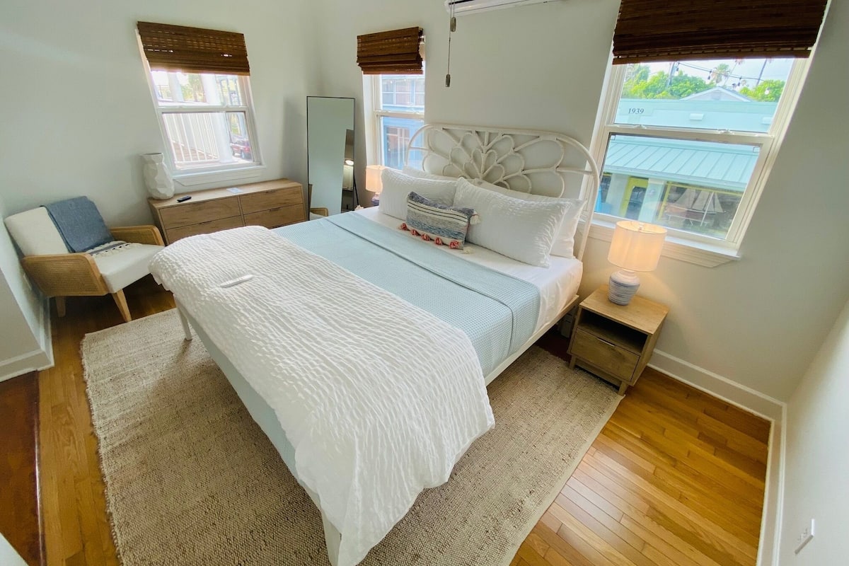 Un dormitorio con una cama, una silla, una mesita de noche, un aparador y una ventana con persianas.