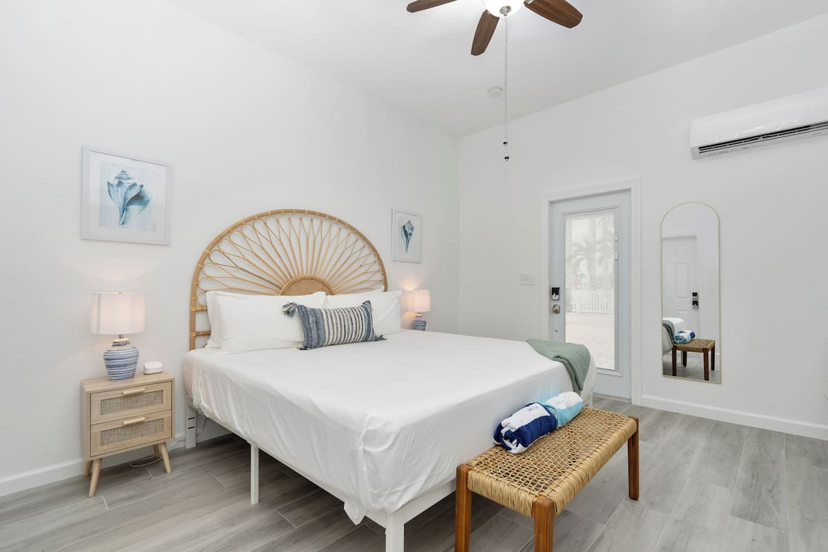 Un dormitorio moderno con una cama grande, mesitas de noche, un banco y un ventilador de techo.