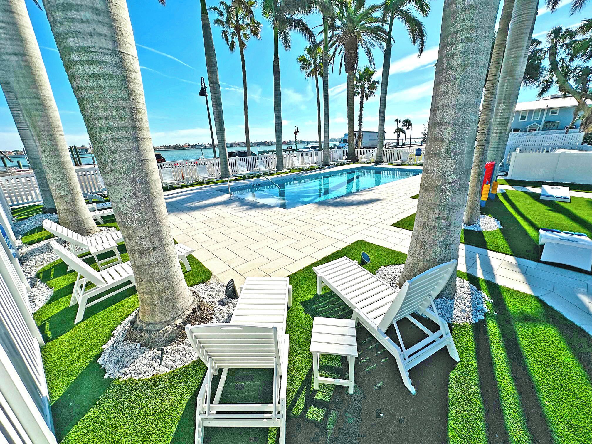 A pool area with white lounge chairs, palm trees, and a view of the water.