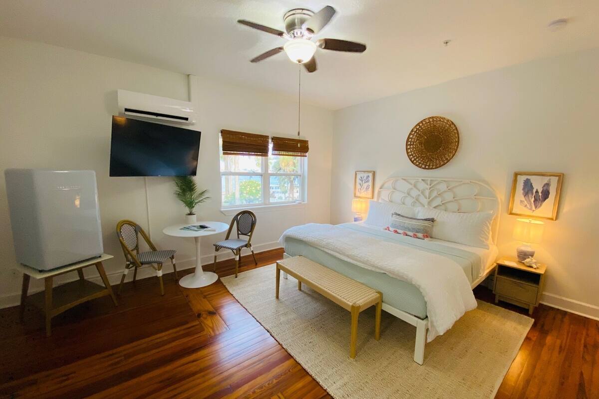 Un dormitorio con cama, escritorio, silla, televisor y ventilador de techo.