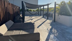 Une terrasse sur le toit avec un hamac, un canapé et un espace ombragé.