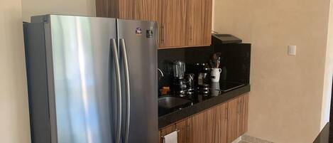 A kitchen with a stainless steel refrigerator, wooden cabinets, a black countertop, and a tiled floor.