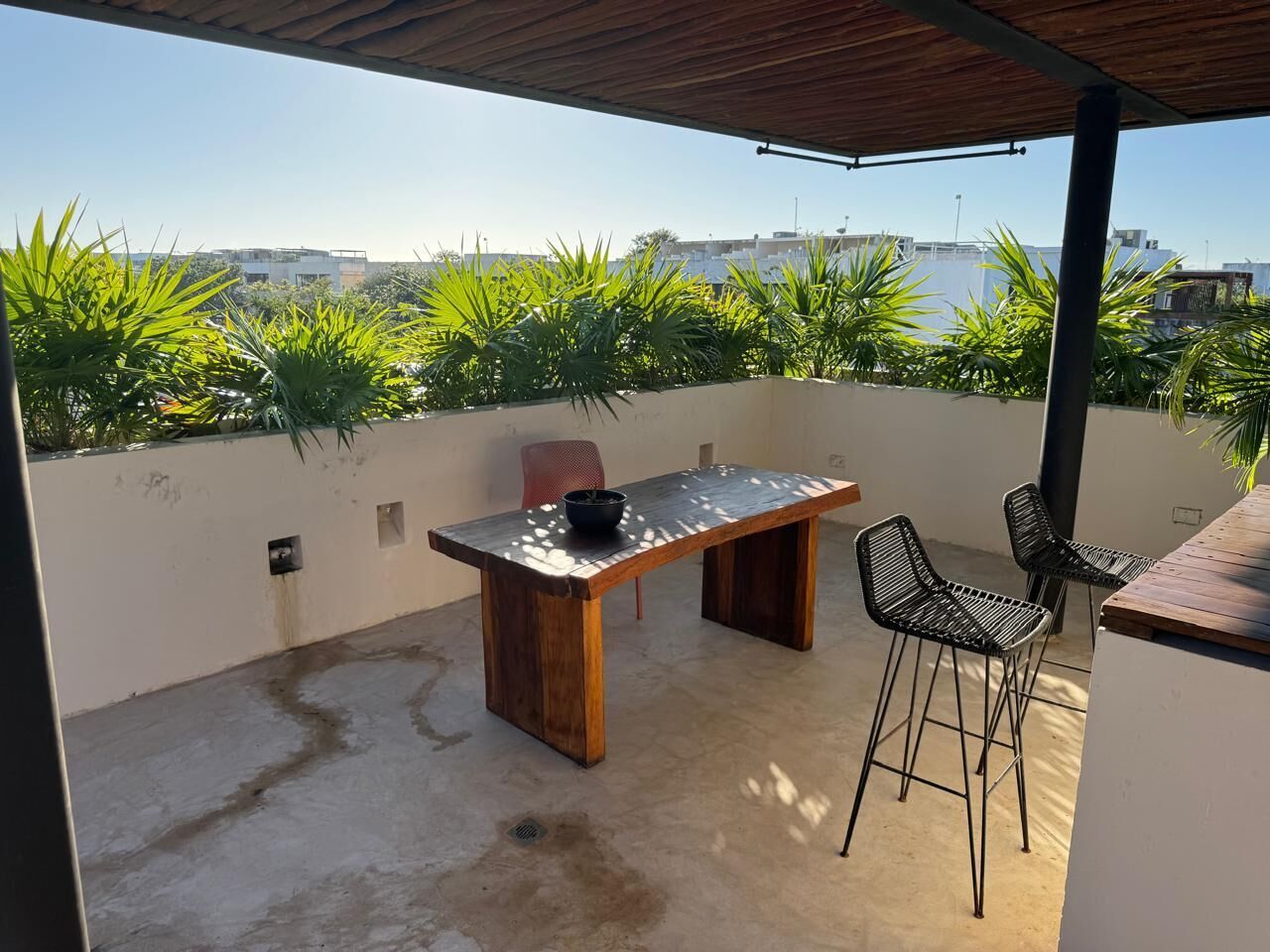 Un patio al aire libre con una mesa de madera y dos sillas, rodeado de plantas verdes exuberantes.