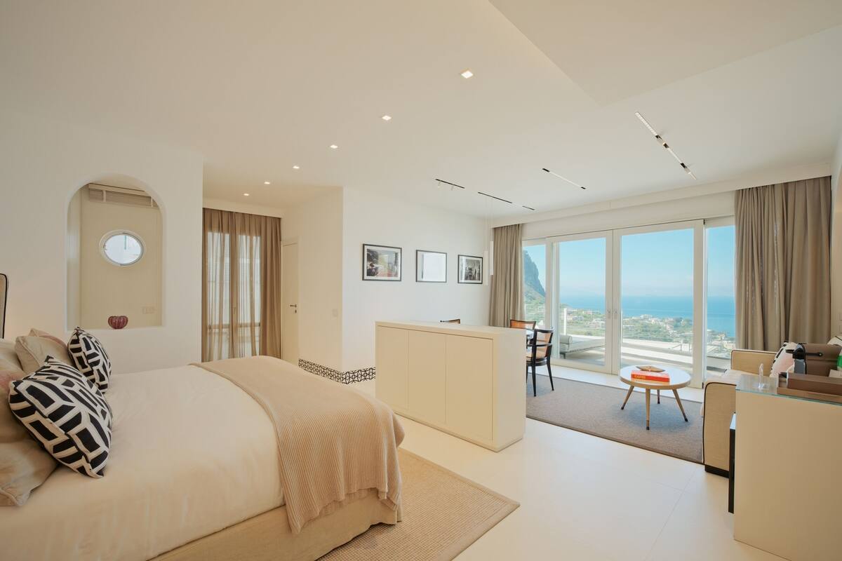 A modern hotel room with a large bed, a desk, and a view of the sea.