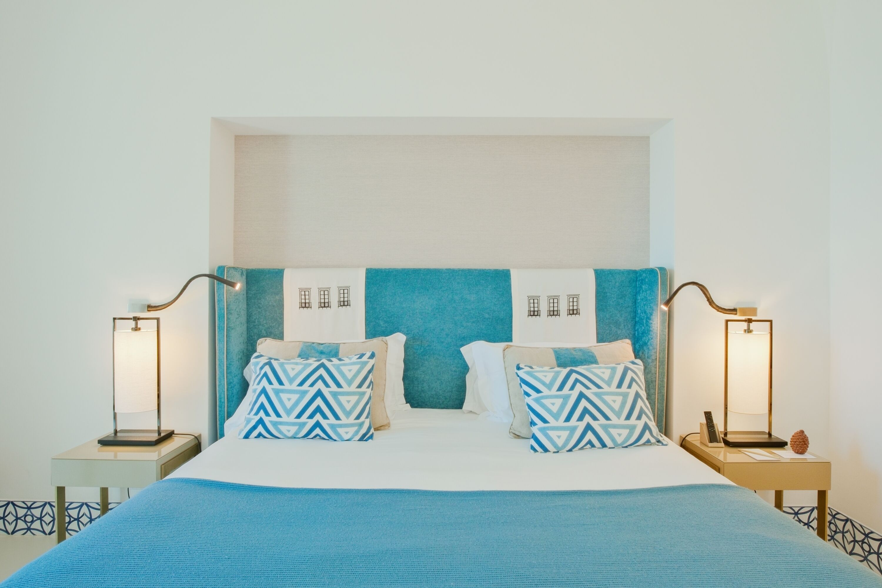 Una cama con cabecera azul, dos mesitas de noche con lámparas y almohadas estampadas.