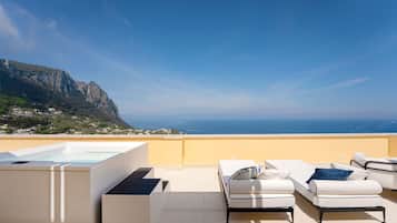 A rooftop terrace with a pool, white lounge chairs, and a view of the ocean and mountains.