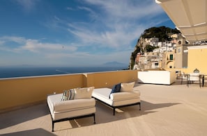 A terrace with two sofas, a table, and chairs, overlooking a coastal town and the sea. - Palazzo M Capri (Capri)