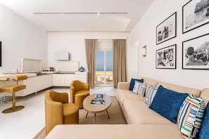A modern hotel room with a sofa, coffee table, and a dining area with chairs and a table. - Palazzo M Capri (Capri)