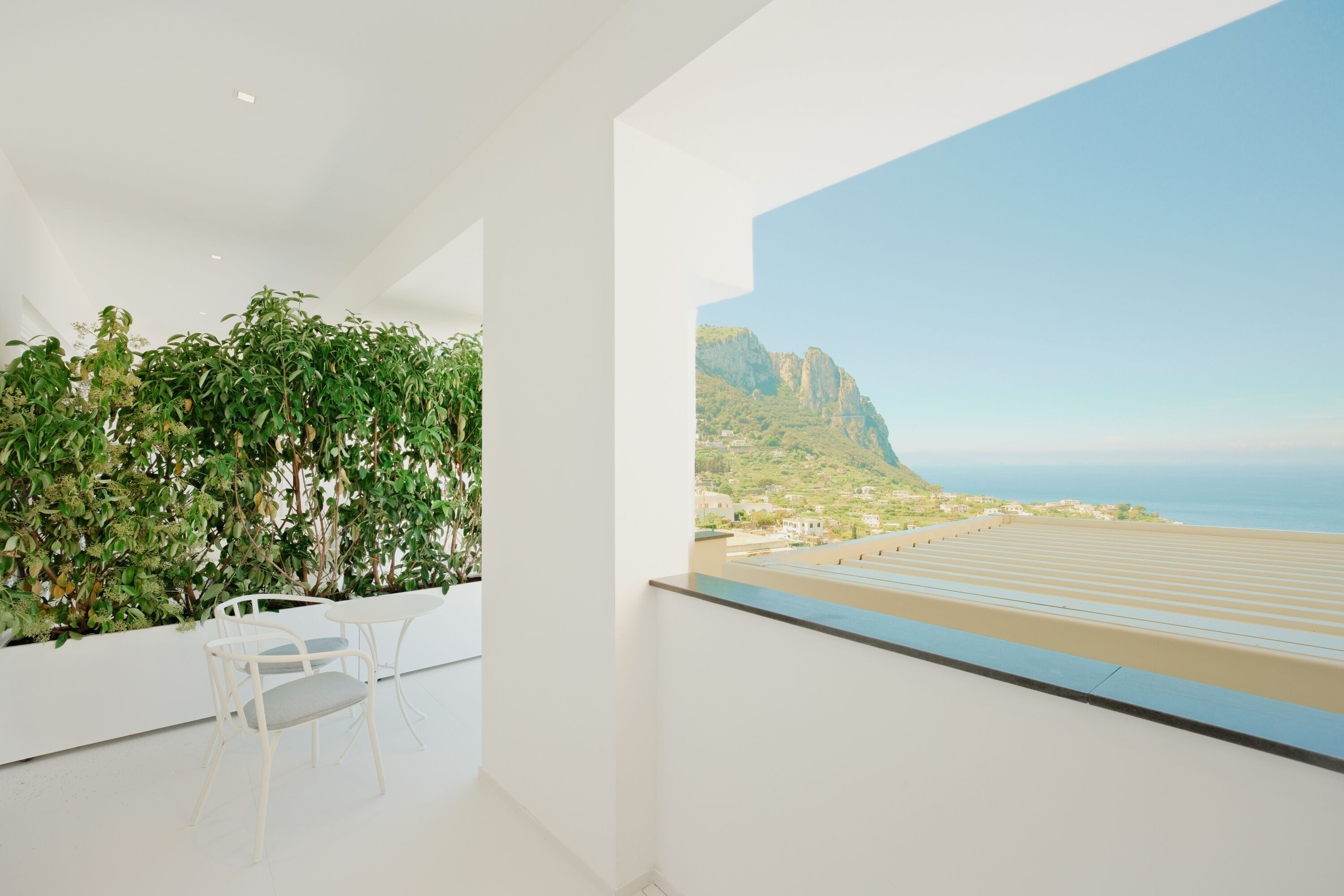 A modern room with a balcony, white walls, and a view of a coastal landscape.