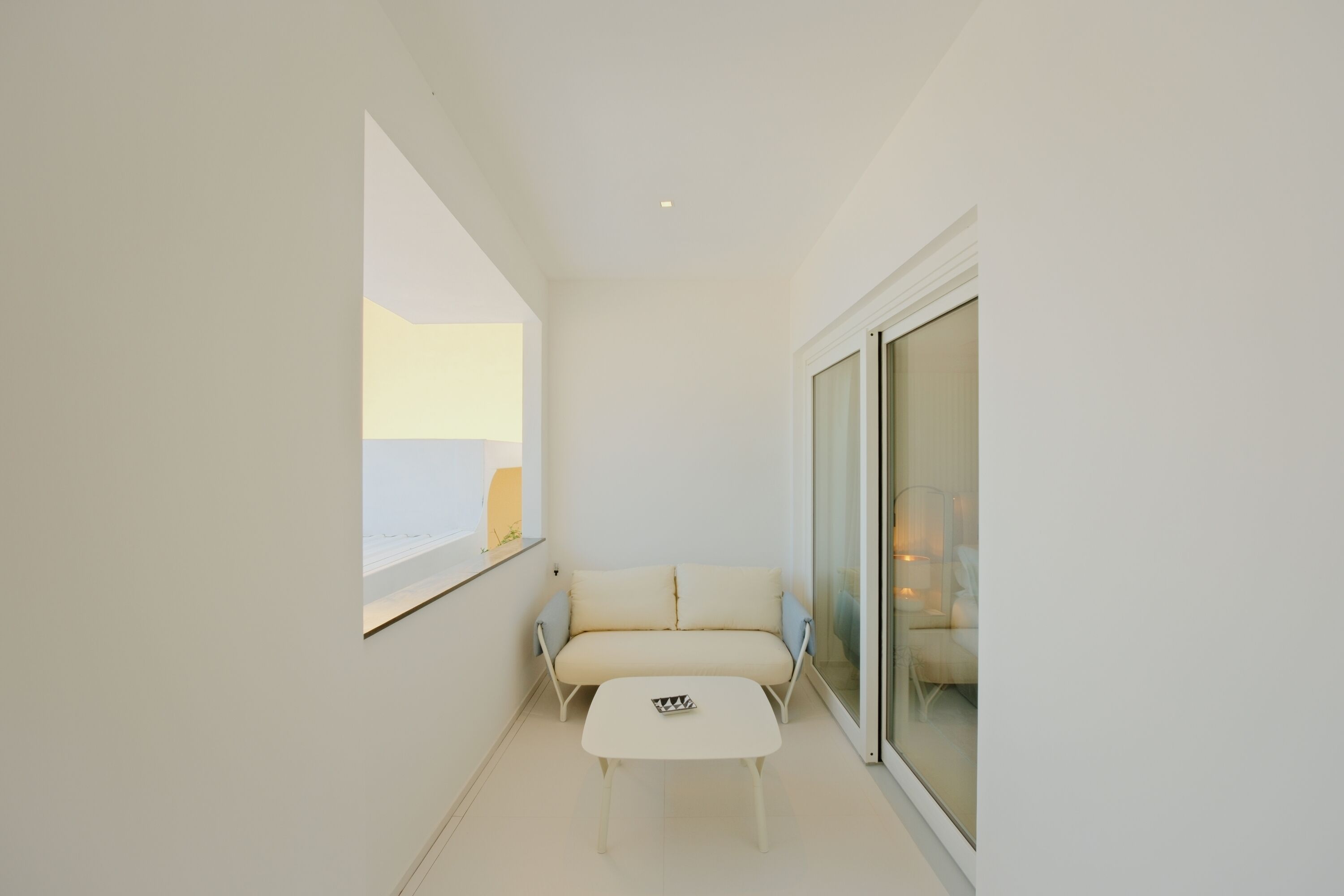 A minimalist room with a white sofa, a small white table, and a large window.