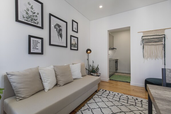 A modern living room with a beige sofa, framed artwork on the wall, and a macrame wall hanging. - Studio with a patio (Lisboa)