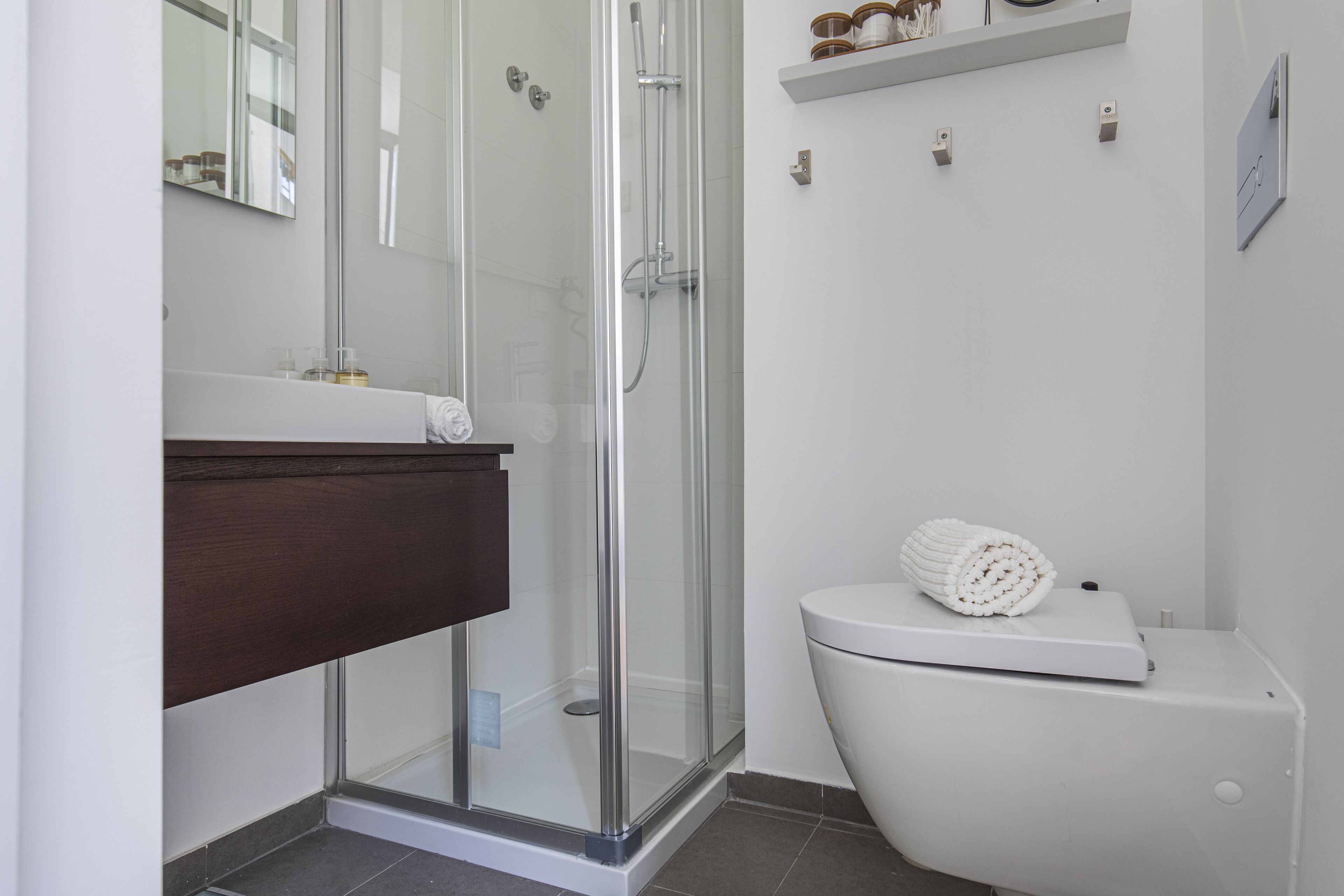 Un baño con ducha de vidrio, inodoro blanco y tocador de madera.