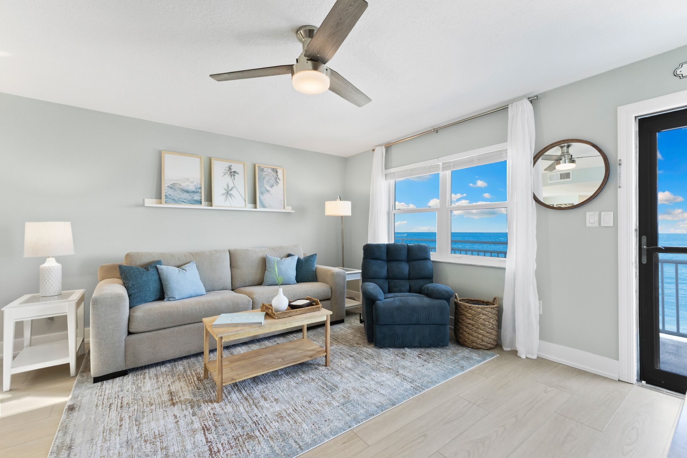 A living room with a sofa, armchair, coffee table, and a view of the ocean through a large window.