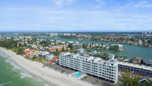 Un hôtel situé sur la côte, doté d’une piscine, offrant une vue sur la plage et donnant sur une marina en arrière-plan.