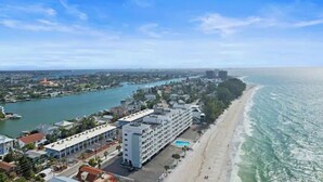 Un hôtel situé sur la côte, avec un long bâtiment attenant à une plage, une piscine et une vue sur la mer.