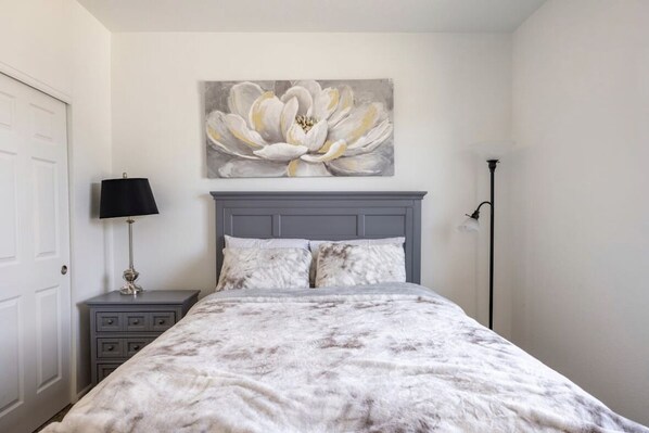 A bedroom with a bed, a nightstand, a lamp, and a painting on the wall.