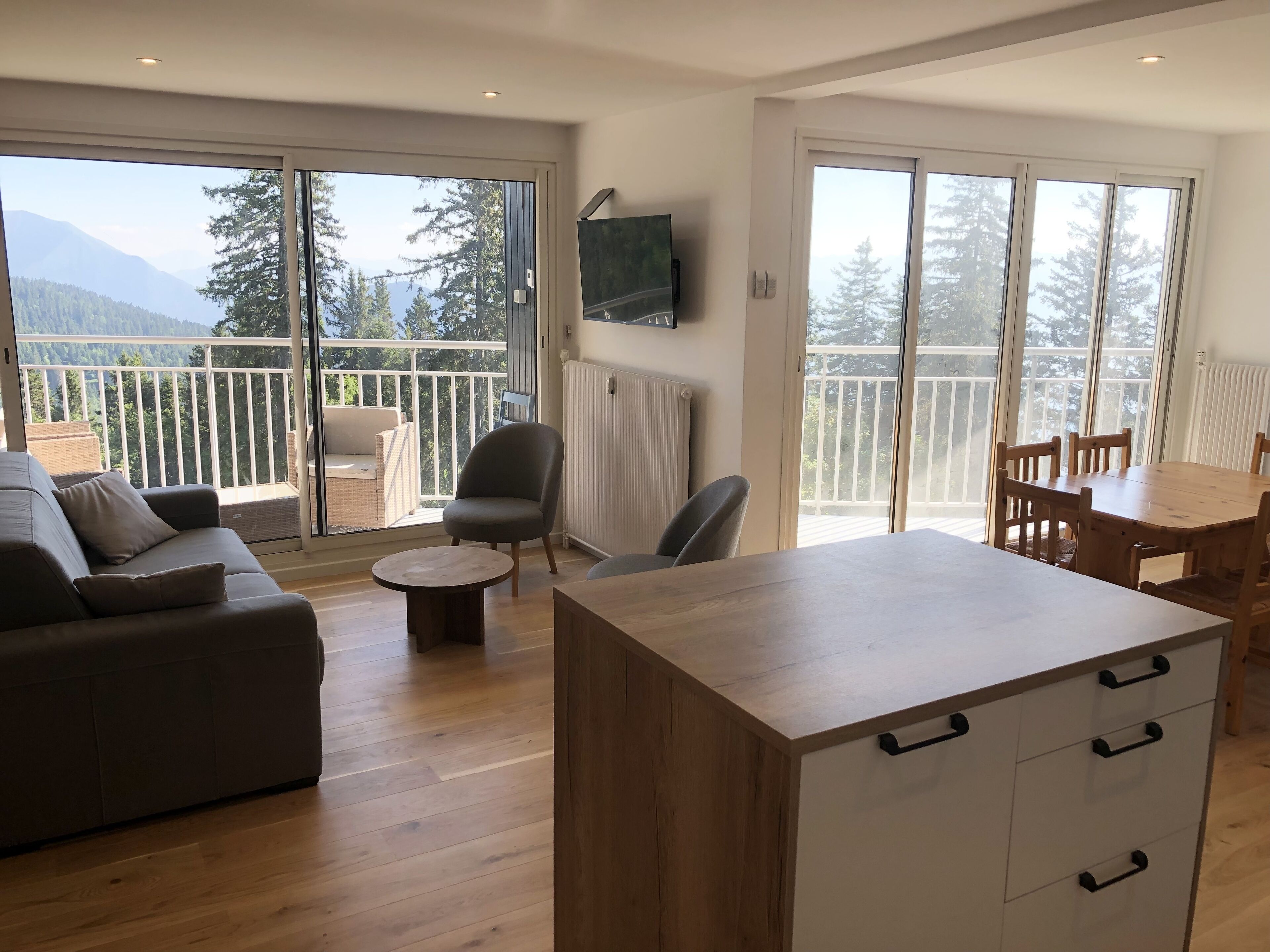 Uma sala de estar moderna com um sofá, uma mesa de centro redonda e uma mesa de jantar de madeira com cadeiras.