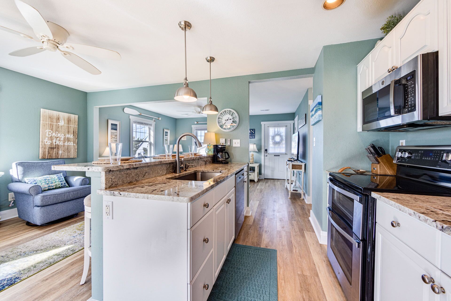 A spacious kitchen with a central island, a dining area with a blue sofa, and a view of the outdoors.