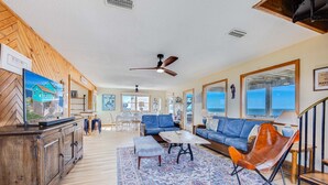 Un salon spacieux avec un grand canapé, une table basse et un tapis à motifs. Un meuble en bois et un téléviseur se trouvent sur le côté gauche.