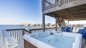 Un bain à remous sur une terrasse en bois, avec vue sur la plage et les maisons en arrière-plan.